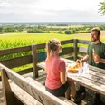 Borgholzhausen-Aussichtsplattform Berghauser Weg-Teutoburger-Wald-Tourismus-D-Ketz-073.jpg Zwei Personen genießen ein Picknick mit Blick auf weite Felder und Wälder von einer Holzplattform.