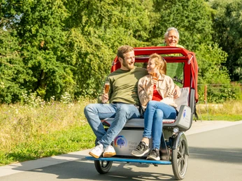 Rheda-Wiedenbrueck-Flora-Westfalica-Park, Rikscha-Fahrt-Teutoburger-Wald-Tourismus-D-Ketz-016.jpg Ein Paar genießt eine gemütliche Rikschafahrt im Park, während der Fahrer lächelnd das Fahrrad steuert.