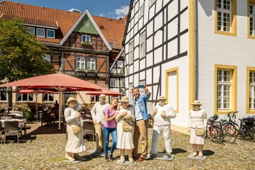 Rheda-Wiedenbrueck-Marktplatz-Teutoburger-Wald-Tourismus-D-Ketz-051.jpg Gruppe von Menschen posiert fröhlich neben lebensgroßen Figuren auf einem gepflasterten Platz.