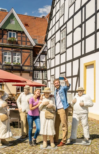 Rheda-Wiedenbrueck-Marktplatz-Teutoburger-Wald-Tourismus-D-Ketz-051.jpg Gruppe von Menschen posiert fröhlich neben lebensgroßen Figuren auf einem gepflasterten Platz.
