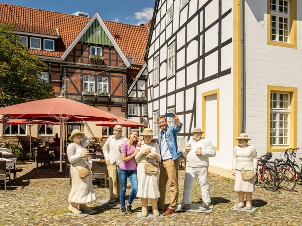 Rheda-Wiedenbrueck-Marktplatz-Teutoburger-Wald-Tourismus-D-Ketz-051.jpg Gruppe von Menschen posiert fröhlich neben lebensgroßen Figuren auf einem gepflasterten Platz.