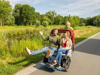 Rheda-Wiedenbrueck-Flora-Westfalica-Park, Rikscha-Fahrt-Teutoburger-Wald-Tourismus-D-Ketz-011.jpg Ein älteres Ehepaar sitzt lachend auf einer Rikscha, die von einem fröhlichen Mann gefahren wird.