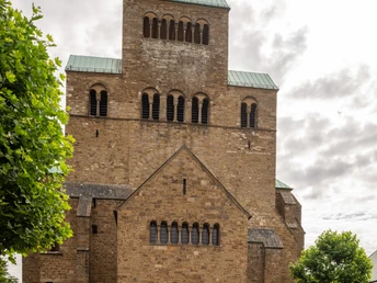 Die Fassade des Mindener Doms mit zwei Radfahrern im Vordergrund unter bewölktem Himmel.