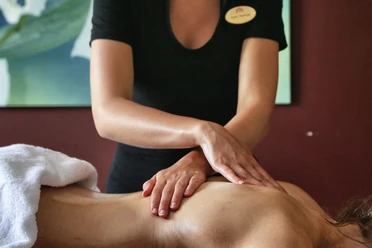 Spa im Gräflichen Park Eine Masseurin in schwarzer Kleidung führt eine Rückenmassage durch; im Hintergrund ist ein abstraktes Bild.
