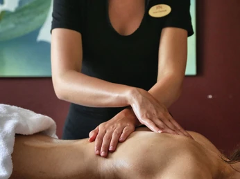 Spa im Gräflichen Park Eine Masseurin in schwarzer Kleidung führt eine Rückenmassage durch; im Hintergrund ist ein abstraktes Bild.