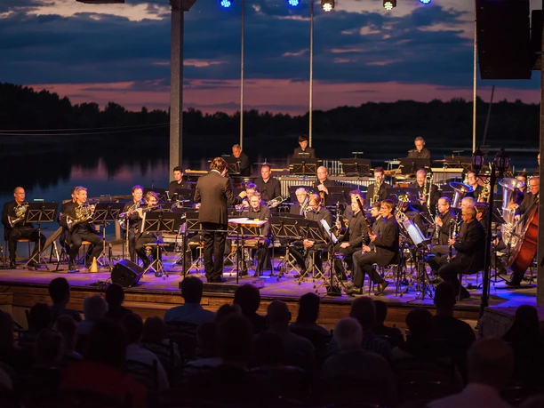 Sächsische Bläserphilharmonie am Biedermeierstrand Konzert der Sächsischen Bläserphilharmonie am Biedermeierstrand am Abend mit See im Hintergrund
