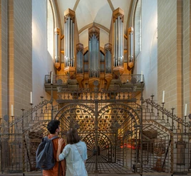 Paderborn-Dom-Teutoburger-Wald-Tourismus-Patrick-Gawandtka-068.jpg Ein Paar betrachtet die imposante Orgel einer historischen Kirche, eingerahmt von kunstvollen Gittern.