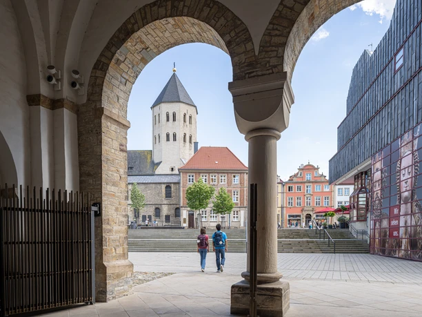 Blick durch einen Torbogen auf den Dom in Osnabrück, zwei Personen spazieren in Richtung des Platzes.