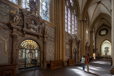 Zwei Personen betrachten kunstvoll verzierte Wände und Glasfenster in einem historischen Kirchenschiff.