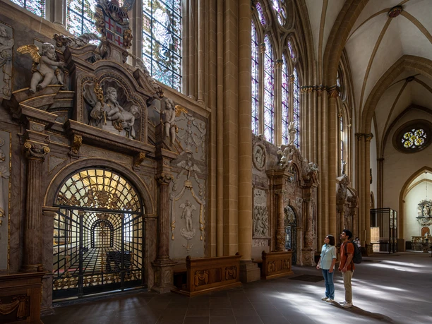 Paderborn-Dom-Teutoburger-Wald-Tourismus-Patrick-Gawandtka-064.jpg Zwei Personen betrachten kunstvoll verzierte Wände und Glasfenster in einem historischen Kirchenschiff.