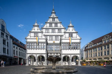 Paderborn-Rathaus-Teutoburger-Wald-Tourismus-Patrick-Gawandtka-095.jpg Ein historisches Rathaus mit markanter Fassade und Brunnen im Vordergrund, bei blauem Himmel gezeigt.