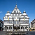 Paderborn-Rathaus-Teutoburger-Wald-Tourismus-Patrick-Gawandtka-095.jpg Ein historisches Rathaus mit markanter Fassade und Brunnen im Vordergrund, bei blauem Himmel gezeigt.