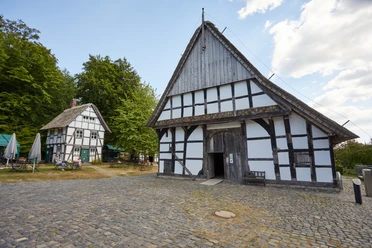 Bielefeld-Bauernhausmuseum-Teutoburger-Wald-Tourismus-T-Evers-049.jpg Fachwerkhäuser des Museums Bauernhaus Bielefeld, umgeben von Bäumen, bei sonnigem Wetter.