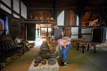 Zwei Personen erkunden ein historisches Bauernhausmuseum, umgeben von alten Küchenutensilien.
