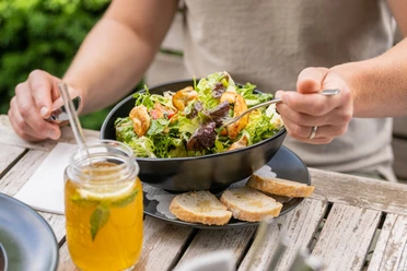 Bielefeld-Bürgerpark-Teutoburger-Wald-Tourismus-D-Ketz-079.jpg Salat mit Garnelen und Brot, serviert auf einem Holztisch, daneben ein Glas mit kaltem Getränk.