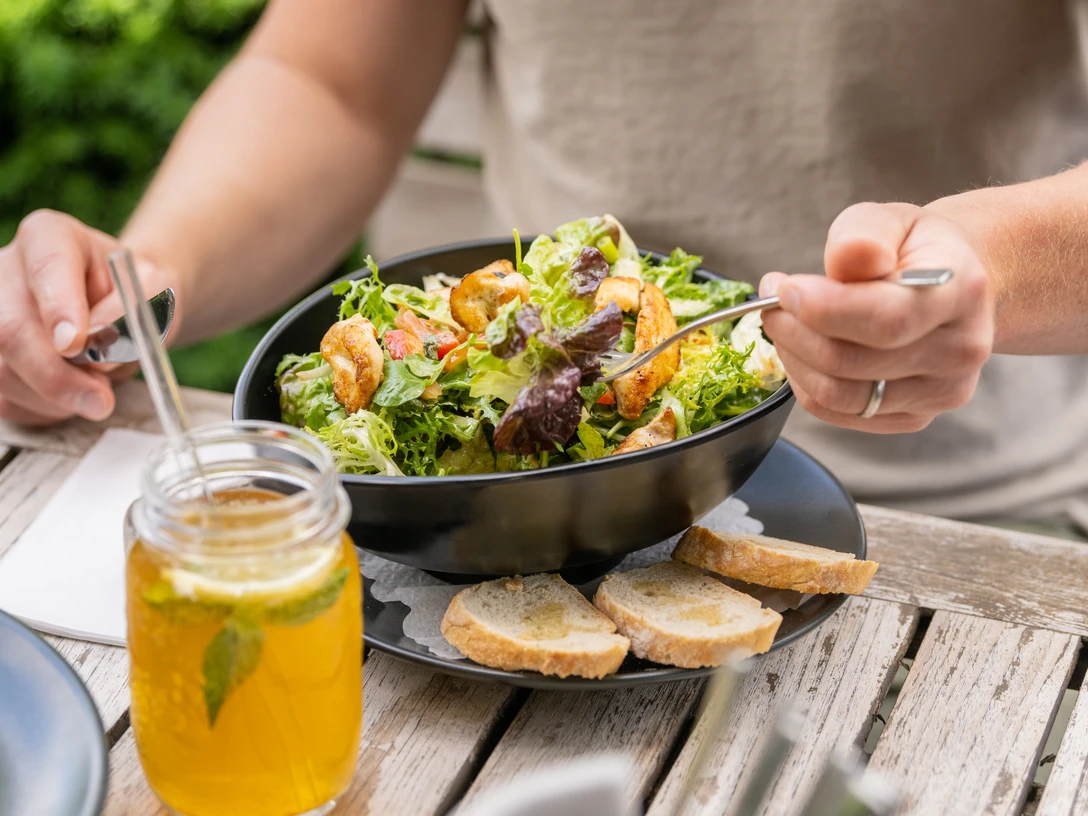 Bielefeld-Bürgerpark-Teutoburger-Wald-Tourismus-D-Ketz-079.jpg Salat mit Garnelen und Brot, serviert auf einem Holztisch, daneben ein Glas mit kaltem Getränk.