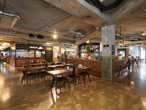 Bielefeld-Harms Markt-Teutoburger-Wald-Tourismus-T-Evers-061.jpg Moderne, industrielle Gastrofläche mit hölzernen Tischen, offener Küche und einladender Beleuchtung.