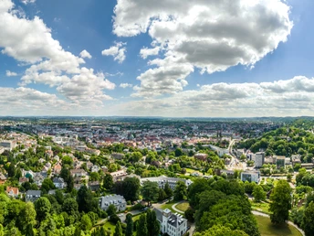 Panoramablick über Bielefeld mit grünen Hügeln, Wäldern, Gebäuden und klarem Himmel mit Wolken.