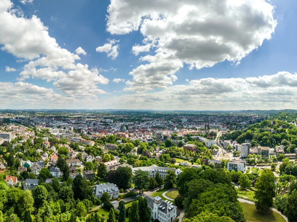 Bielefeld-Johannisberg-Teutoburger-Wald-Tourismus-D-Ketz-046.jpg Panoramablick über Bielefeld mit grünen Hügeln, Wäldern, Gebäuden und klarem Himmel mit Wolken.