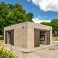 Öffentliche Toilettenanlage in einem Park, umgeben von Bäumen und grünem Laubwerk.