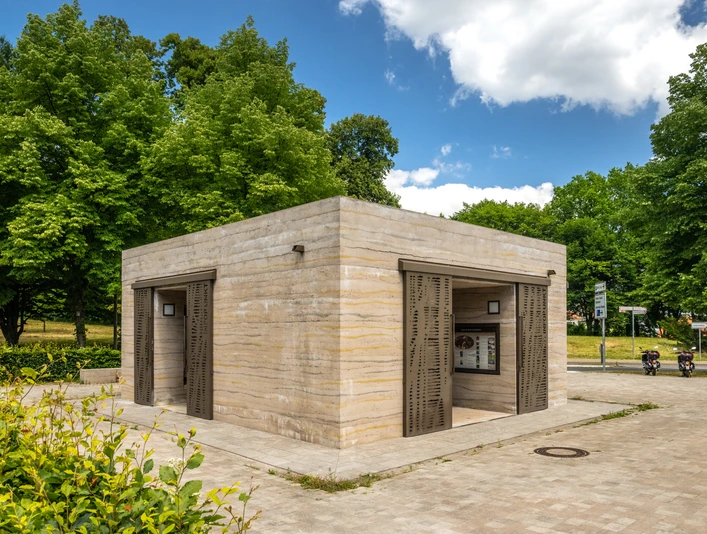 Öffentliche Toilettenanlage in einem Park, umgeben von Bäumen und grünem Laubwerk.