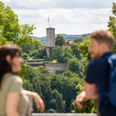 Bielefeld-Johannisberg-Teutoburger-Wald-Tourismus-D-Ketz-049.jpg Ein Paar genießt den Blick auf eine Burgruine, umgeben von üppigem Grün bei sonnigem Wetter.