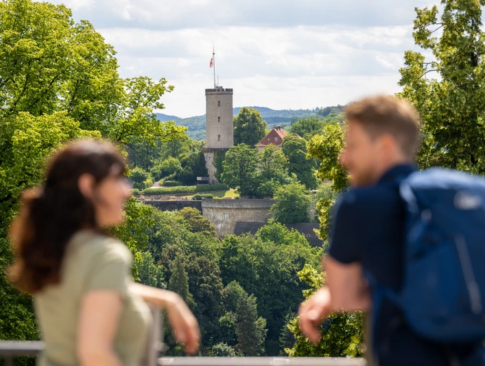 Bielefeld-Johannisberg-Teutoburger-Wald-Tourismus-D-Ketz-049.jpg Ein Paar genießt den Blick auf eine Burgruine, umgeben von üppigem Grün bei sonnigem Wetter.