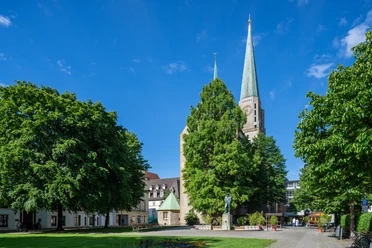 Die Altstädter Nicolaikirche in Bielefeld, umgeben von Bäumen und einem sonnigen blauen Himmel.