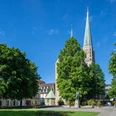 Die Altstädter Nicolaikirche in Bielefeld, umgeben von Bäumen und einem sonnigen blauen Himmel.