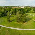 <p>Weitläufiger Park mit Rasenflächen, Bäumen und Wegen, Menschen entspannen im Grünen.</p>