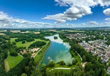 Bielefeld-Obersee-Teutoburger-Wald-Tourismus-D-Ketz-053.jpg Luftaufnahme eines Sees inmitten grüner Landschaft und Wohngebieten in Bielefeld unter blauem Himmel.