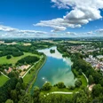 Bielefeld-Obersee-Teutoburger-Wald-Tourismus-D-Ketz-053.jpg Luftaufnahme eines Sees inmitten grüner Landschaft und Wohngebieten in Bielefeld unter blauem Himmel.