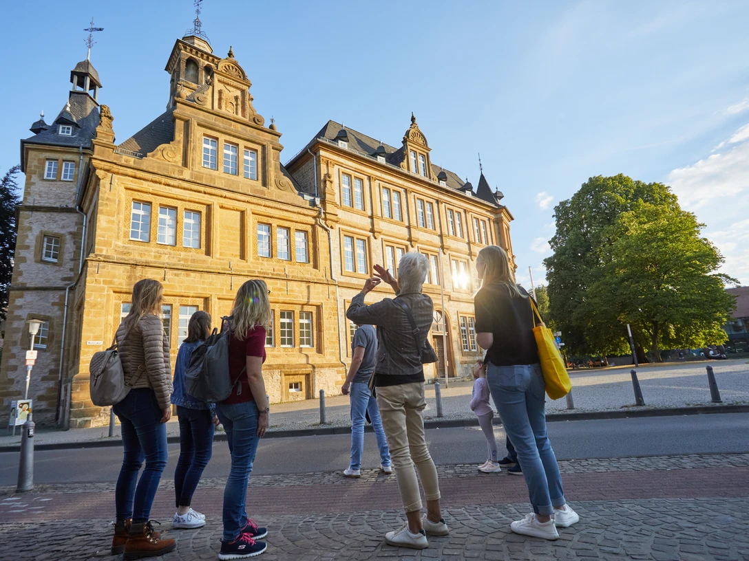 Bielefeld-Ratsgymnasium-Stadtführung-Teutoburger-Wald-Tourismus-T-Evers-092.jpg Gruppe von Touristen besichtigt ein historisches Gebäude in Bielefeld bei Sonnenuntergang.