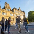 Bielefeld-Ratsgymnasium-Stadtführung-Teutoburger-Wald-Tourismus-T-Evers-092.jpg Gruppe von Touristen besichtigt ein historisches Gebäude in Bielefeld bei Sonnenuntergang.