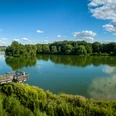 Bielefeld-Obersee-Teutoburger-Wald-Tourismus-D-Ketz-070.jpg Eine hölzerne Aussichtsplattform überblickt einen ruhigen See mit Enten, umgeben von grünen Bäumen.
