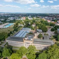 Luftaufnahme eines historischen Gebäudes inmitten grüner Landschaft unter blauem Himmel mit Wolken.