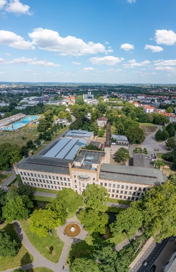 Luftaufnahme eines historischen Gebäudes inmitten grüner Landschaft unter blauem Himmel mit Wolken.