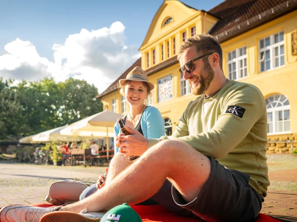 Bielefeld-Siegfriedplatz (Siggi)-Teutoburger-Wald-Tourismus-D-Ketz-082.jpg <p>Ein junges Paar sitzt entspannt auf einer roten Decke vor einem historischen gelben Gebäude.</p>