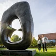 Bielefeld-Skulpturenpark-Teutoburger-Wald-Tourismus-D-Ketz-055.jpg Skulptur mit Loch, im Vordergrund lächelndes Paar, moderne Architektur im Hintergrund, sonniger Tag.