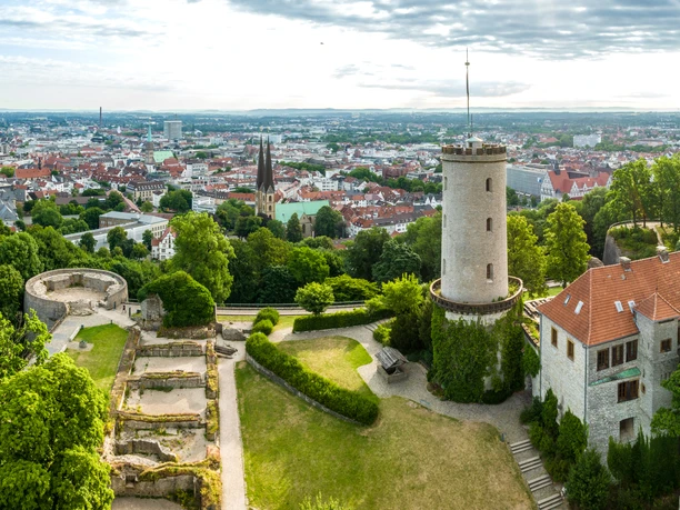 Blick auf die Sparrenburg in Bielefeld, umgeben von grünen Bäumen und einer weiten Stadtlandschaft.