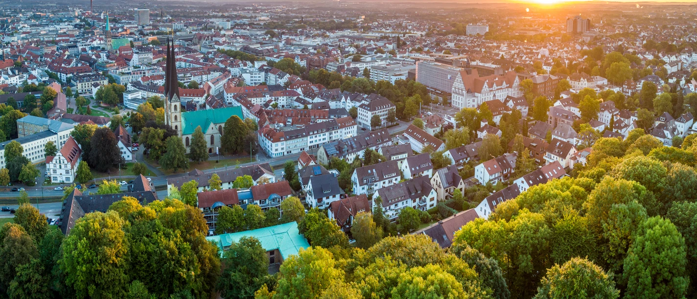 Bielefeld-Sparrenburg-Teutoburger-Wald-Tourismus-D-Ketz-012.jpg <p>Luftaufnahme einer Stadt bei Sonnenuntergang mit Kirche, Wohnhäusern und Bäumen im Vordergrund.</p>