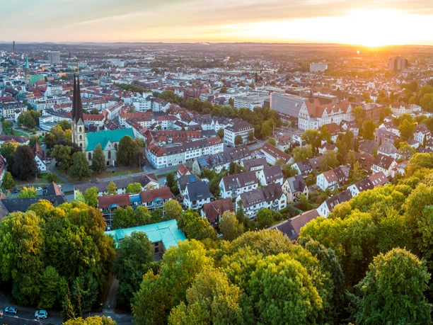 Bielefeld-Sparrenburg-Teutoburger-Wald-Tourismus-D-Ketz-012.jpg <p>Luftaufnahme einer Stadt bei Sonnenuntergang mit Kirche, Wohnhäusern und Bäumen im Vordergrund.</p>