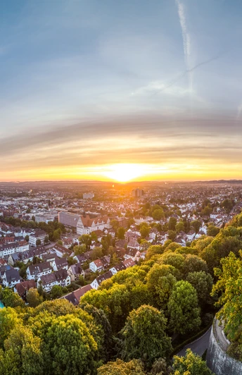 Panorama von Bielefeld bei Sonnenuntergang, mit grünen Hügeln und der Stadt im Tal eingebettet.