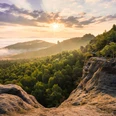 Blick vom Gohrisch Sonnenaufgang über bewaldeten Hügeln, Felsen im Vordergrund, Wolken am Horizont.Sunrise over wooded hills, rocks in the foreground, clouds on the horizon.Východ slunce nad zalesněnými kopci, skály v popředí, mraky na obzoru.Wschód słońca nad zalesionymi wzgórzami, skały na pierwszym planie, chmury na horyzoncie.Zonsopgang boven beboste heuvels, rotsen op de voorgrond, wolken aan de horizon.Alba su colline boscose, rocce in primo piano, nuvole all'orizzonte.
