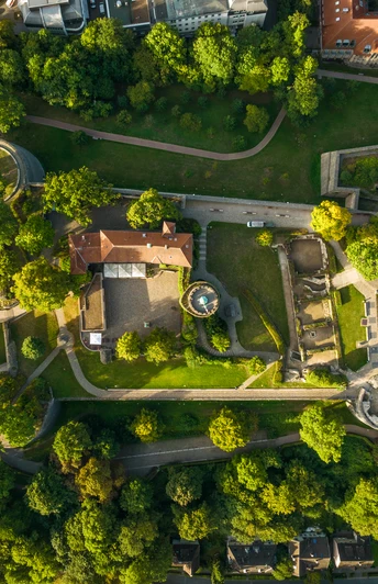 Burganlage mit grünen Bäumen von oben, Wege schlängeln sich durch die Landschaft.