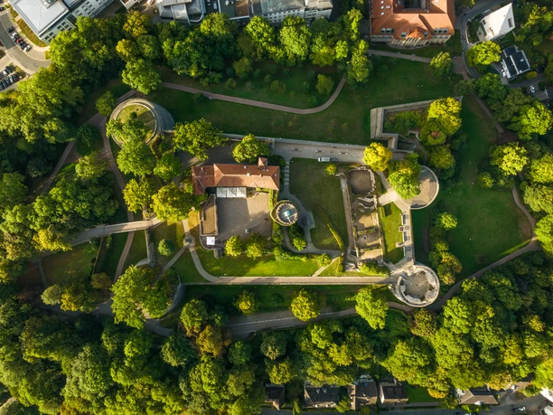 Burganlage mit grünen Bäumen von oben, Wege schlängeln sich durch die Landschaft.