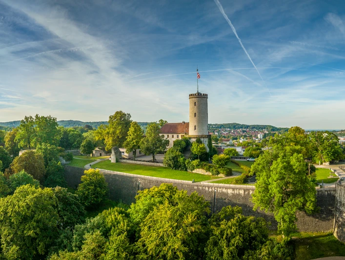 Bielefeld-Sparrenburg-Teutoburger-Wald-Tourismus-D-Ketz-046.jpg Die Sparrenburg in Bielefeld thront majestätisch auf einem bewaldeten Hügel unter blauem Himmel.