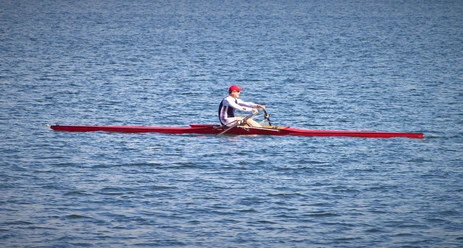 Ruderregatta (2).jpg Blick auf den See, ein Mann sitzt in einem Ruderboot auf dem Wasser.
