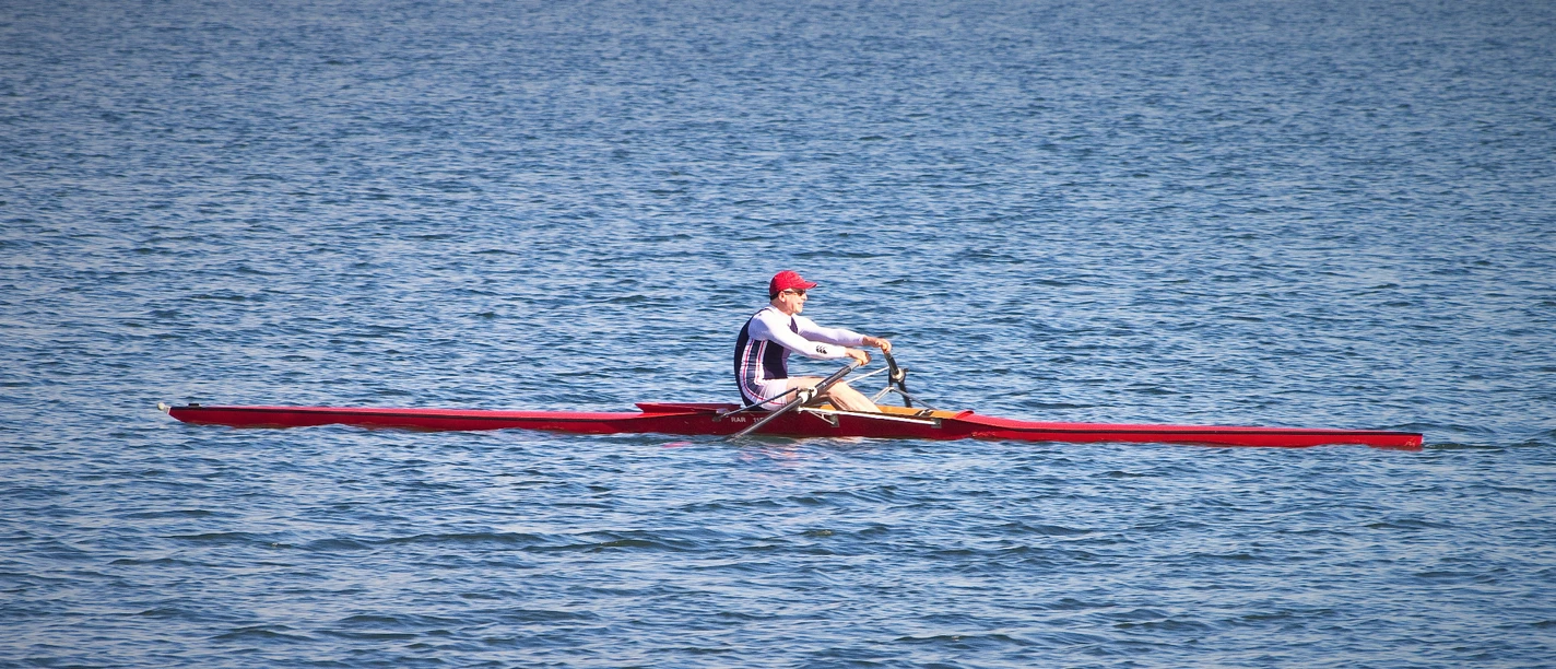 Ruderregatta (2).jpg Blick auf den See, ein Mann sitzt in einem Ruderboot auf dem Wasser.