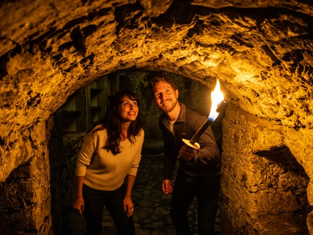 Bielefeld-Sparrenburg-Teutoburger-Wald-Tourismus-D-Ketz-036.jpg Eine Frau und ein Mann erkunden lachend mit Fackel die historischen Gewölbe eines alten Steingemäuers.